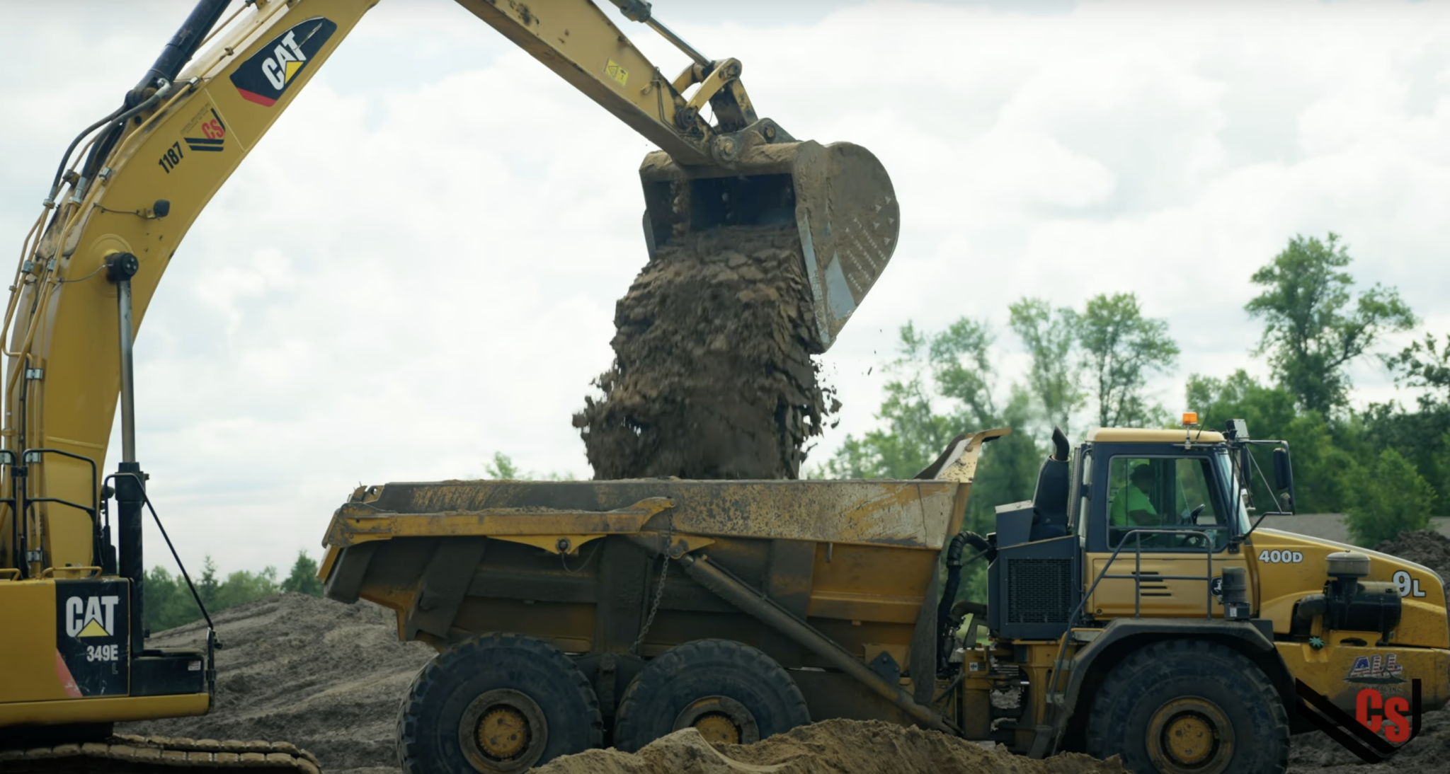 video still with dumptruck being filled by backhoe